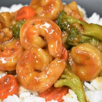 A close up image of shrimp and vegetable stir fry on a bed of white rice.