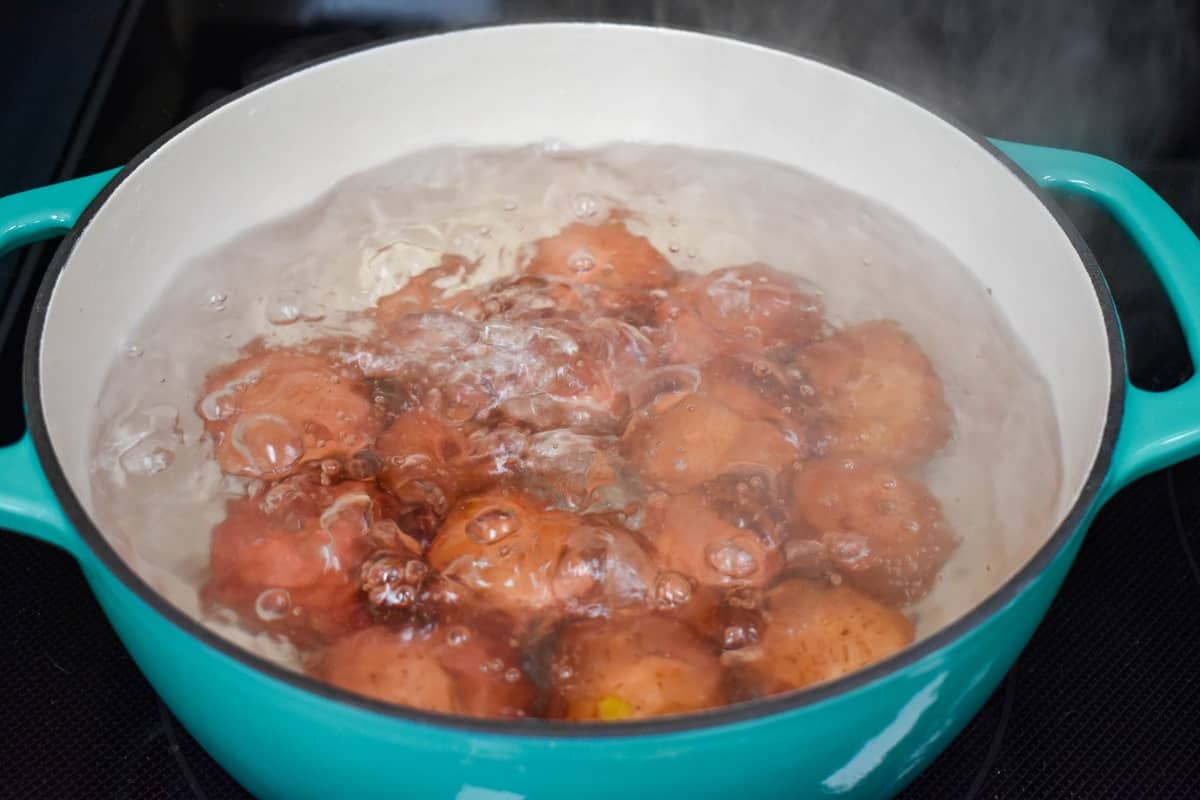 Red potatoes in boiling water in a large teal and white pot.