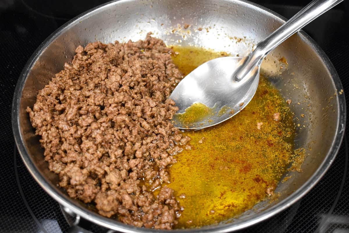 Ground beef and oil in a skillet with a large spoon.