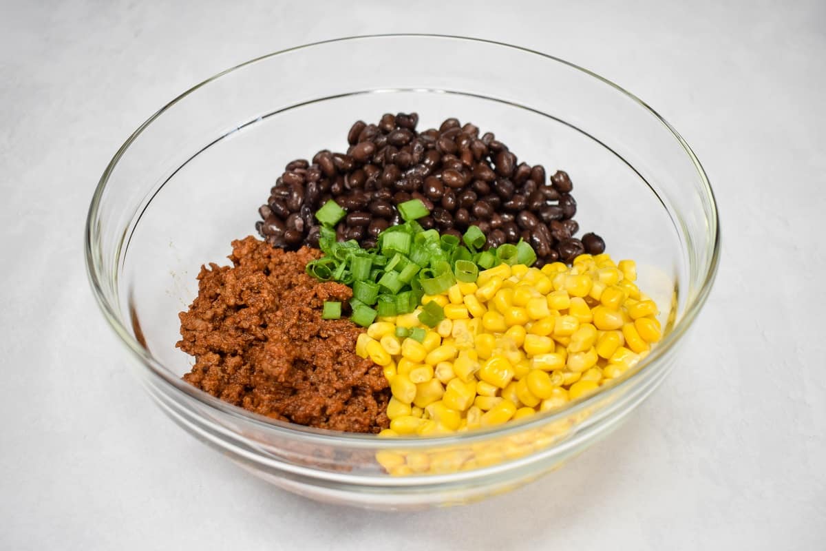 Cooked ground beef, black beans, corn, and green onions in a large, glass bowl.