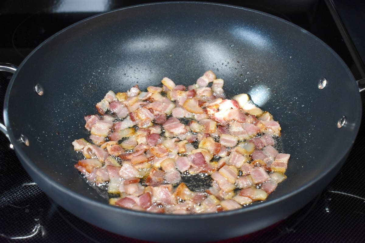 Chopped bacon that is not fully cooked in a large, black skillet.