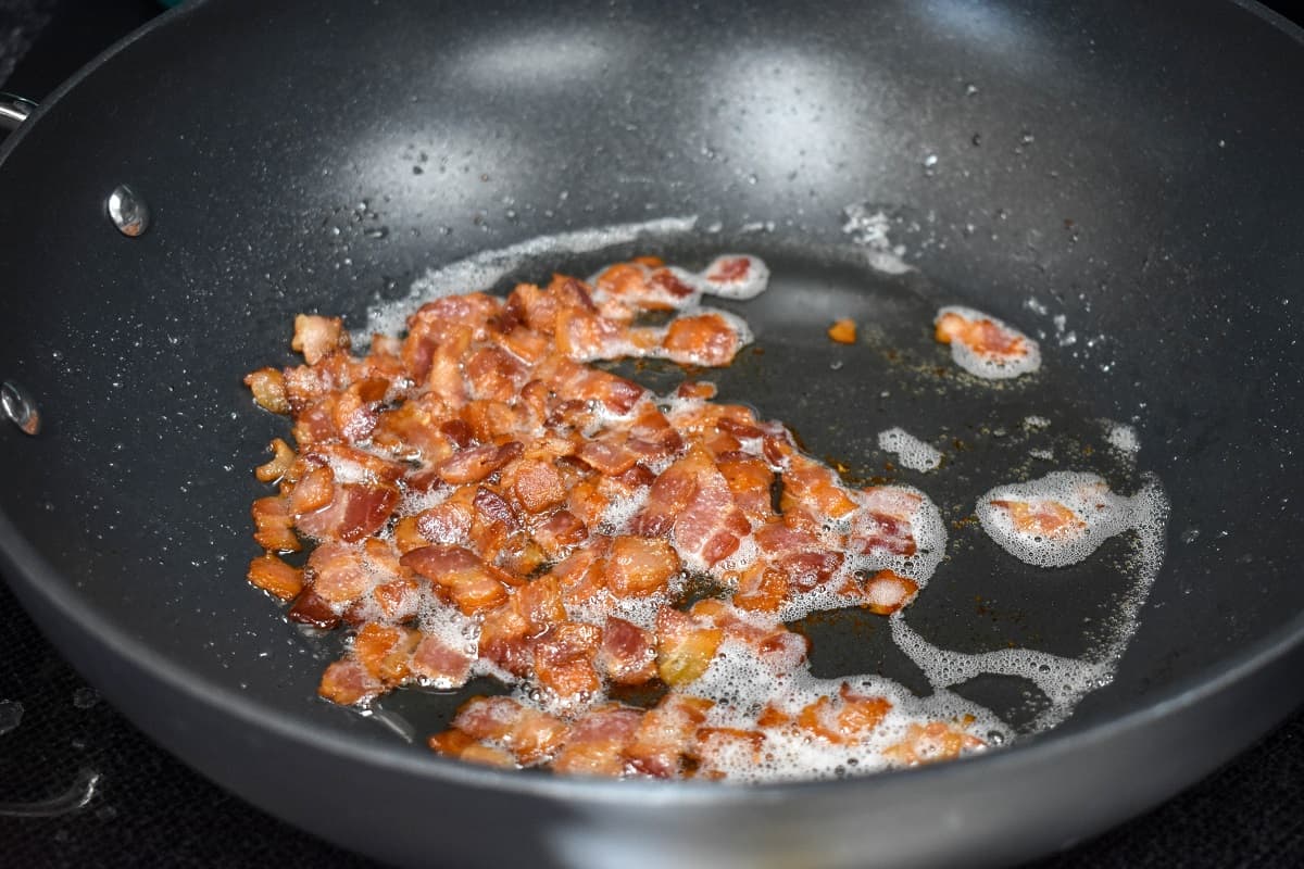 Crispy chopped bacon still in the drippings in a large, black skillet.