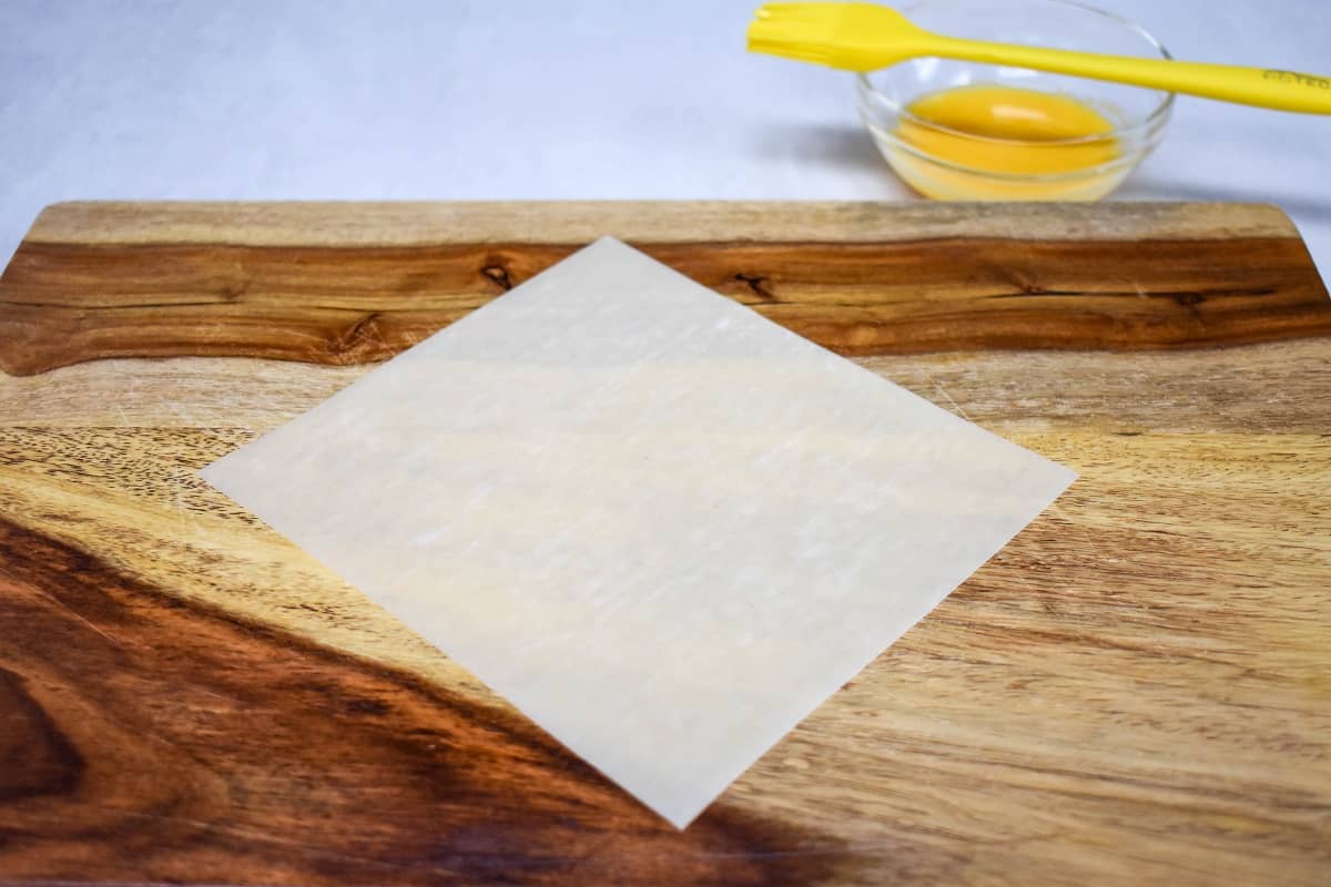 One egg roll wrapper on a wood cutting board.