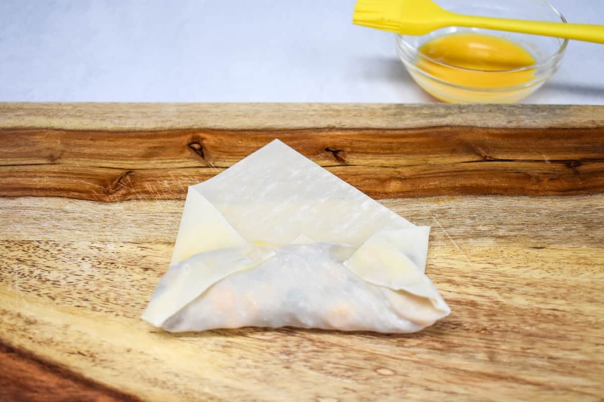 The egg roll with the ends folded in, set on a wood cutting board.