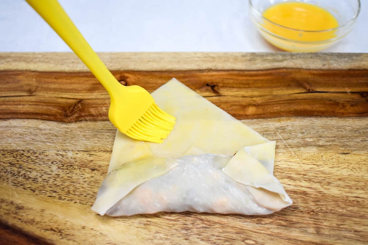 A yellow silicone brush being used to add egg to the exposed area of the egg roll.