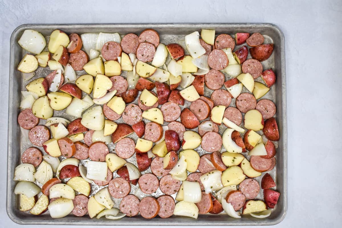 The sausage potato mixture arranged in a single layer on a metal baking sheet.