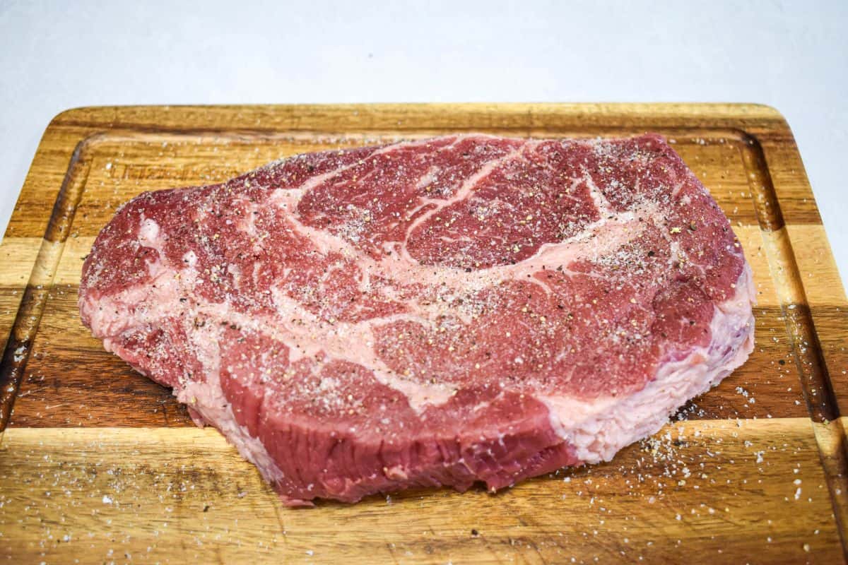 Boneless beef chuck roast seasoned with salt and black pepper on a cutting board.