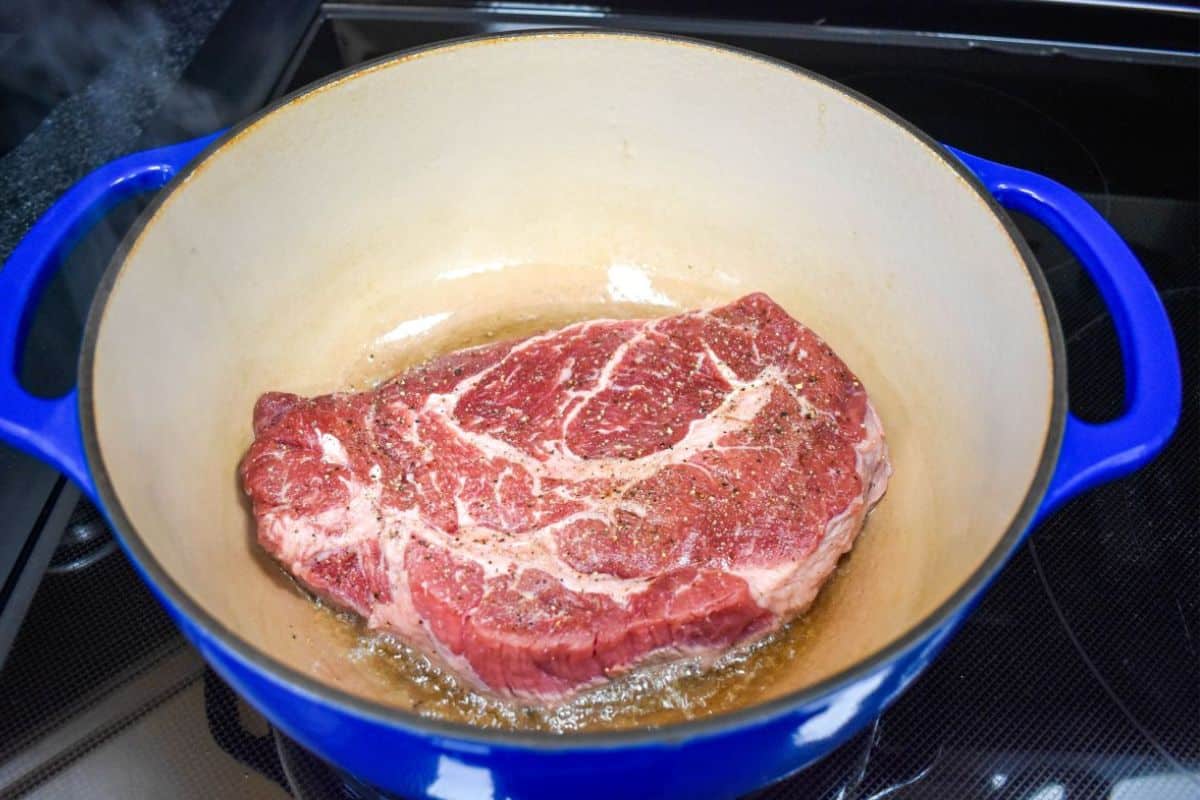 Seasoned beef chuck roast browning in oil in a Dutch oven.