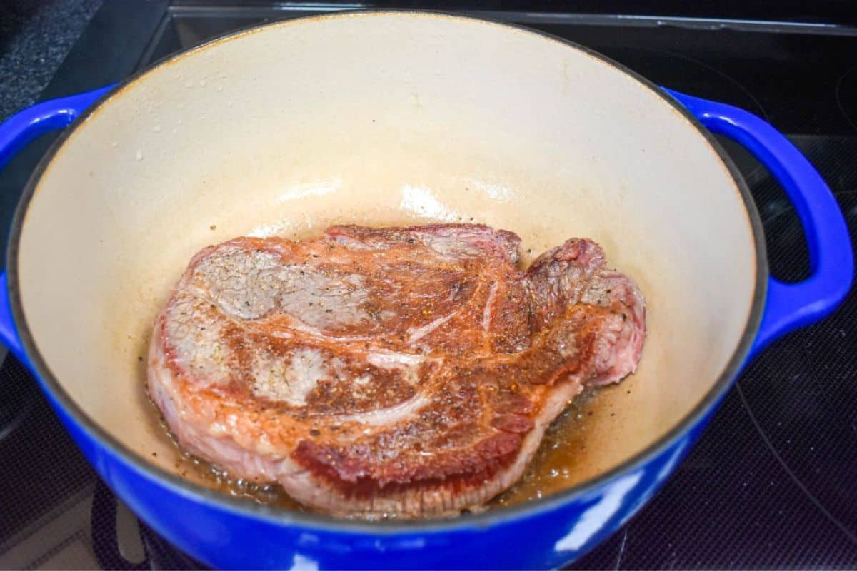 Beef chuck roast browned on one side in a Dutch oven.