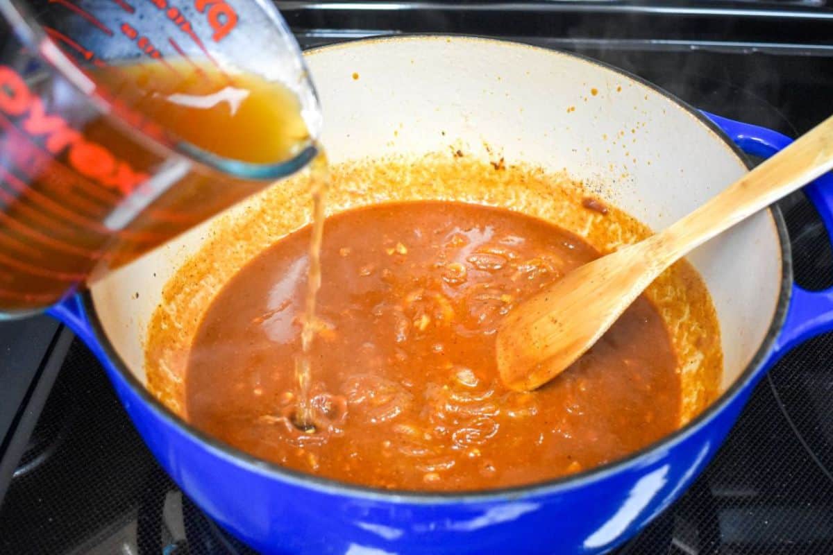 Beef broth being added to the tomato sauce and seasonings in a Dutch oven.