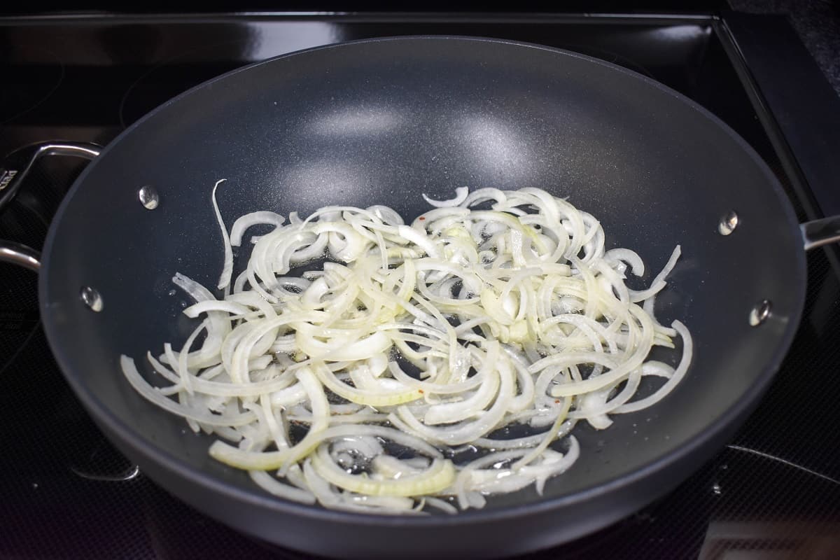 Sliced onions cooking in a large, black skillet.