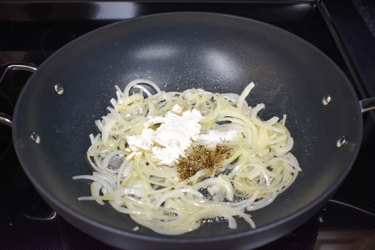 Flour, salt and pepper added to sliced onions in a large black skillet.