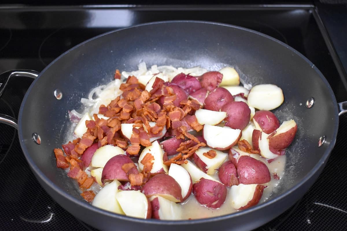 The cut potatoes and bacon added to the sauce in the skillet.