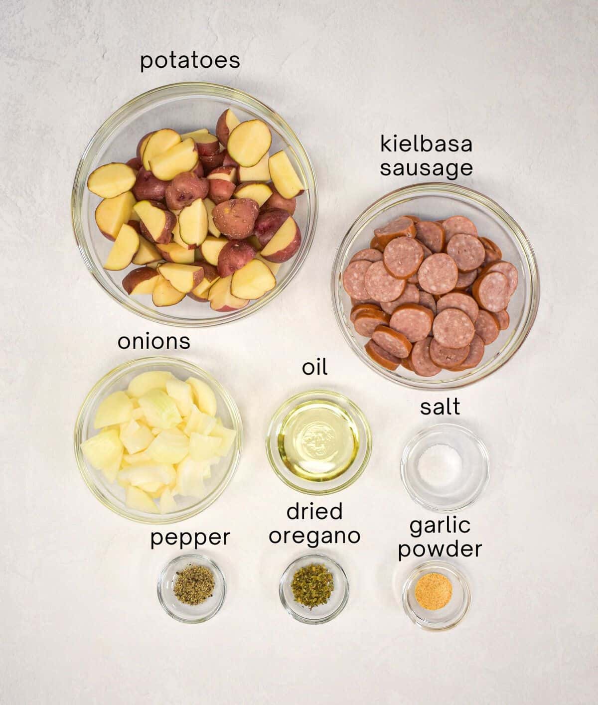 The ingredients for the sheet pan potatoes and sausage prepped and arranged in glass bowls on a table.