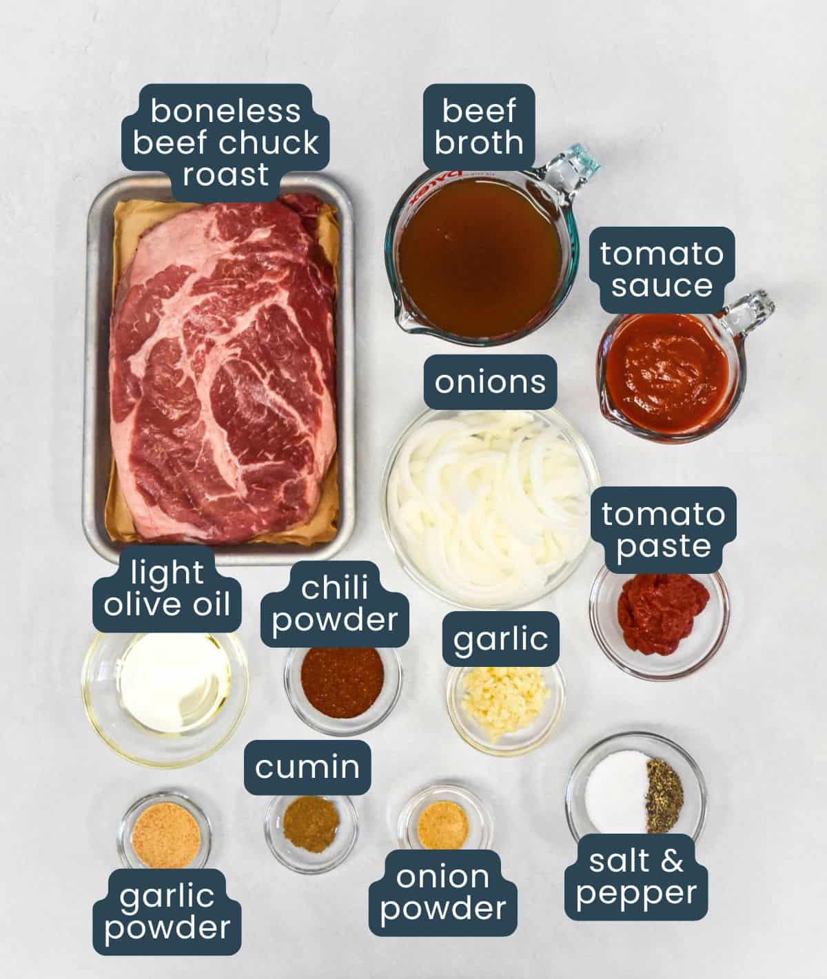 Ingredients for shredded beef tacos including boneless beef chuck roast, beef broth, tomato sauce, onion, garlic, tomato paste, olive oil, and seasonings, with each labeled.