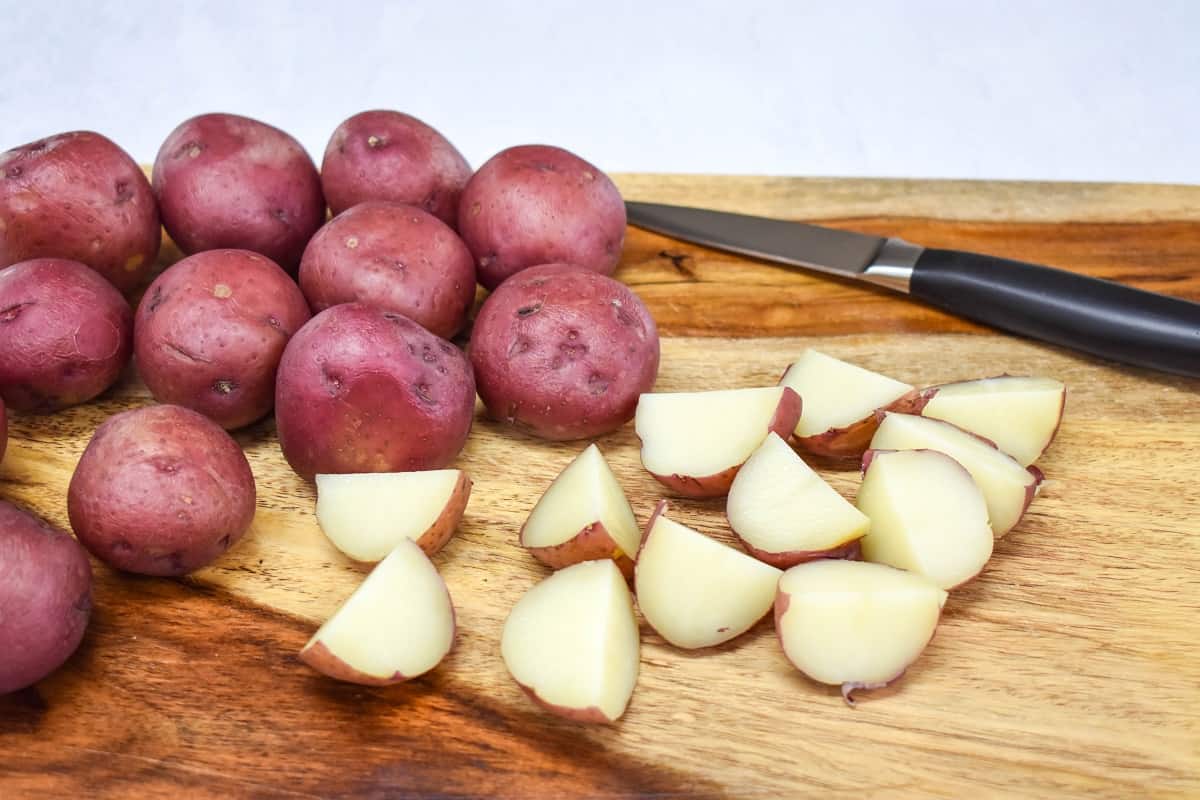 Cooked red potatoes being cut into quarters on a wood cutting board.
