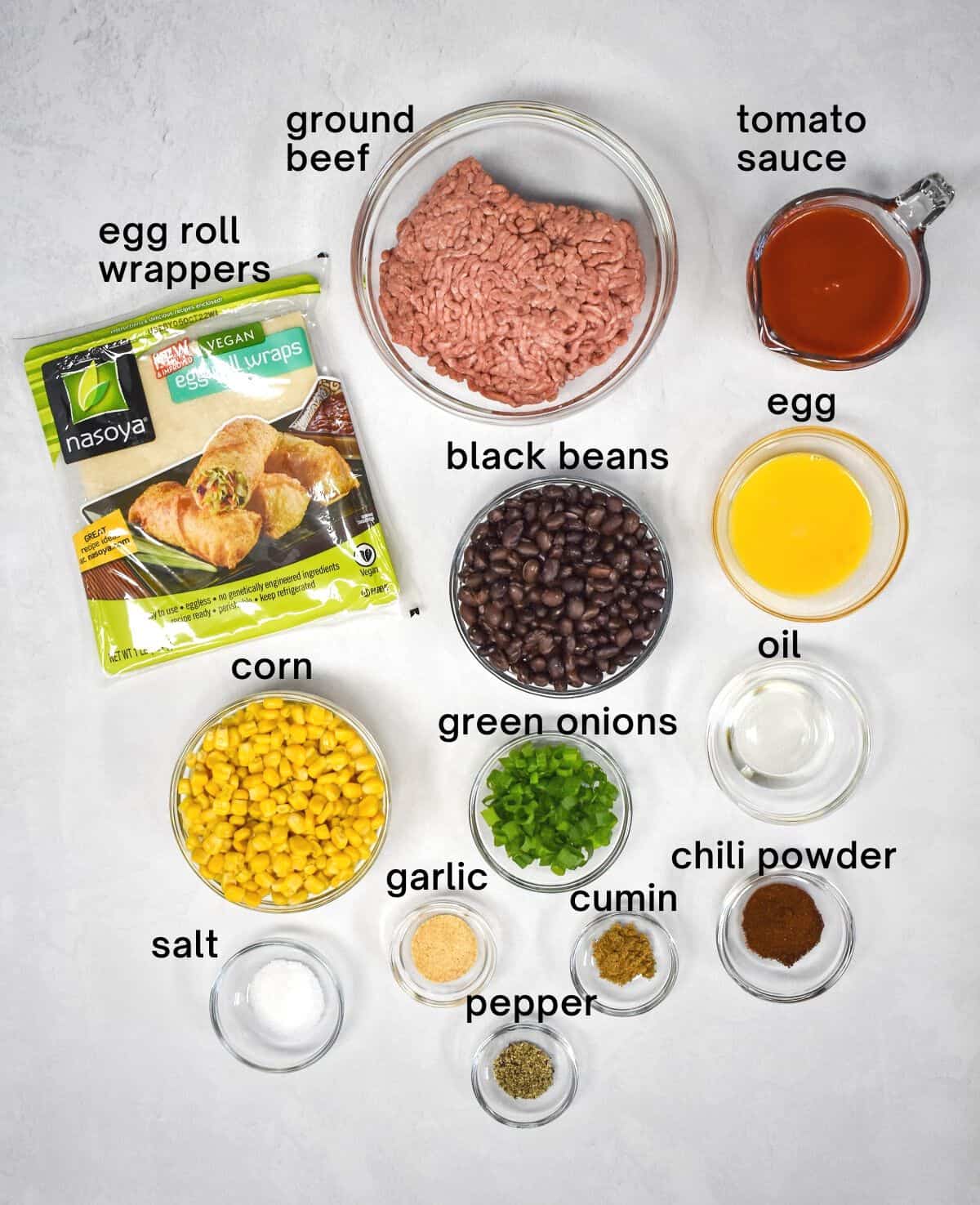 The ingredients for the southwestern egg rolls arranged on a white table with each labeled in small, black letters.