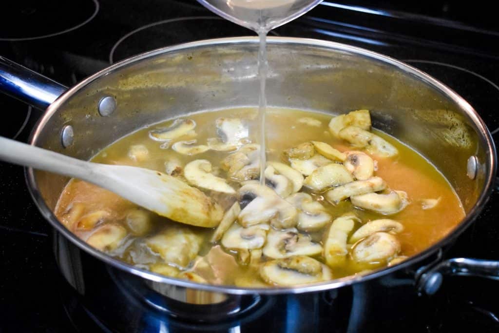 Chicken broth being added to sliced mushrooms in a large skillet.