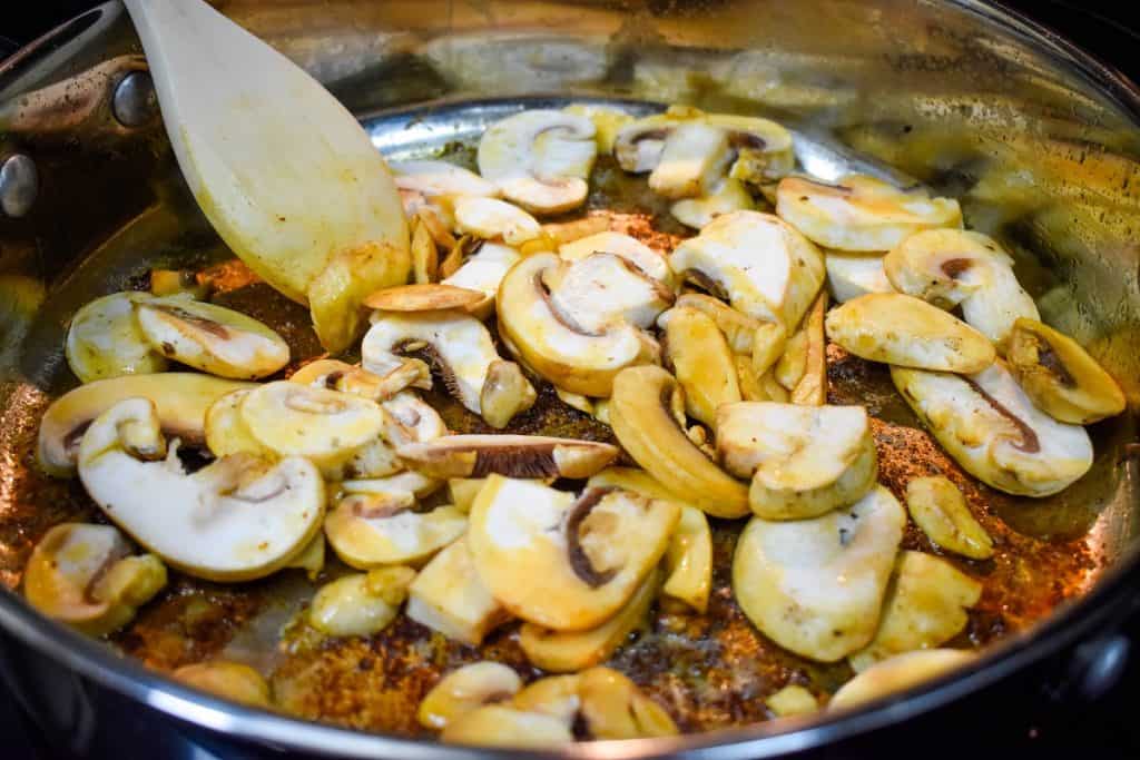 Sliced mushrooms being cooked in a large skillet.