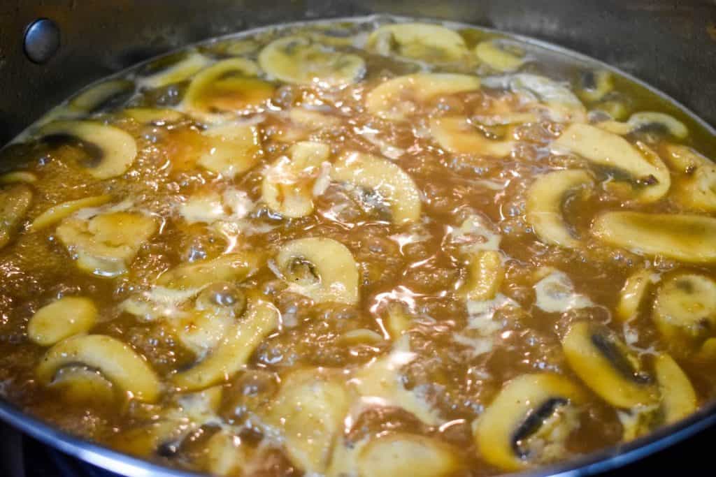 Sliced mushrooms simmering in chicken broth.