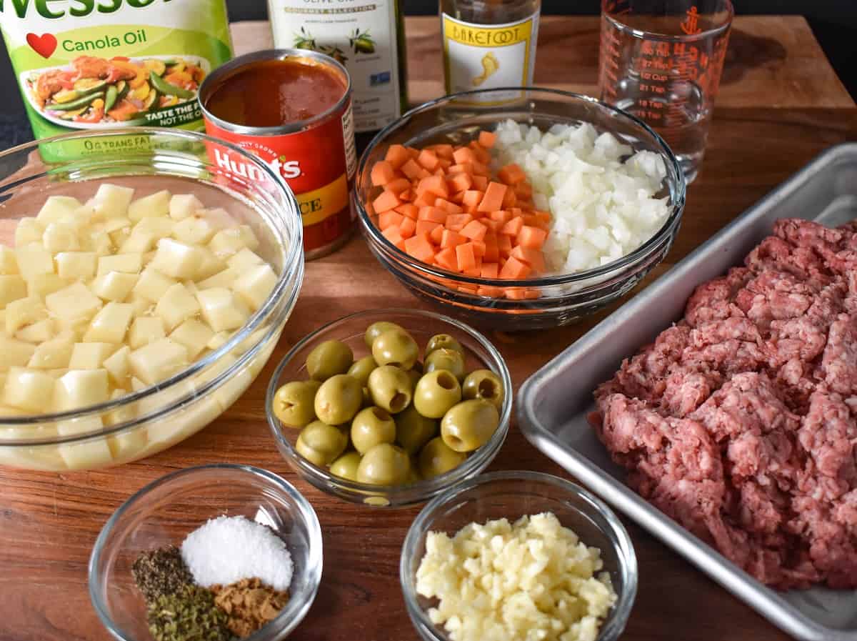 The prepped ingredients for the picadillo arranged on a wood cutting board.