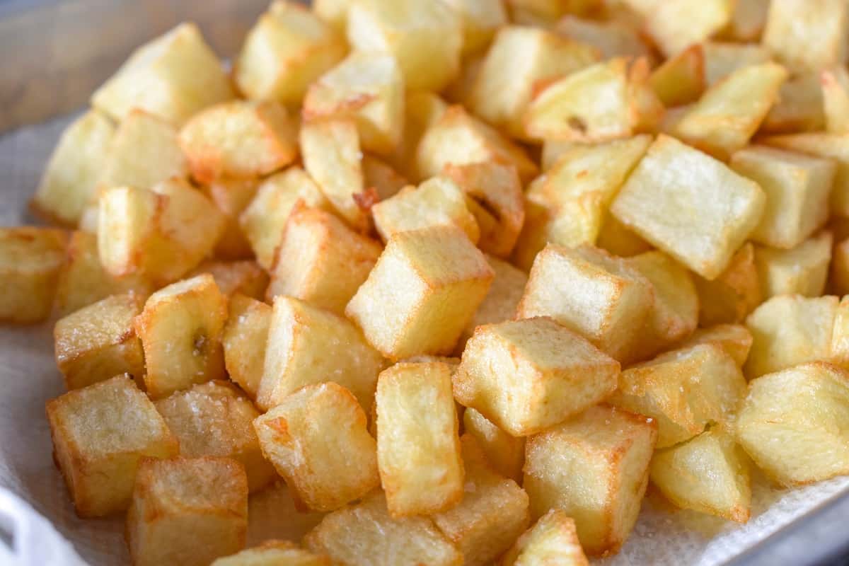 Diced fried potatoes draining on a white paper towel.