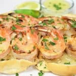 Two grilled shrimp skewers and butter lime sauce served on toasted bread on a white plate and garnished with parsley.