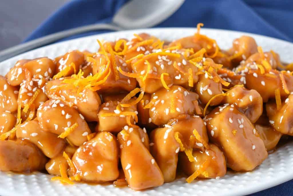 Orange chicken served on a white platter on a blue linen.