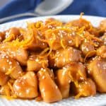 Orange chicken served on a white platter on a blue linen.