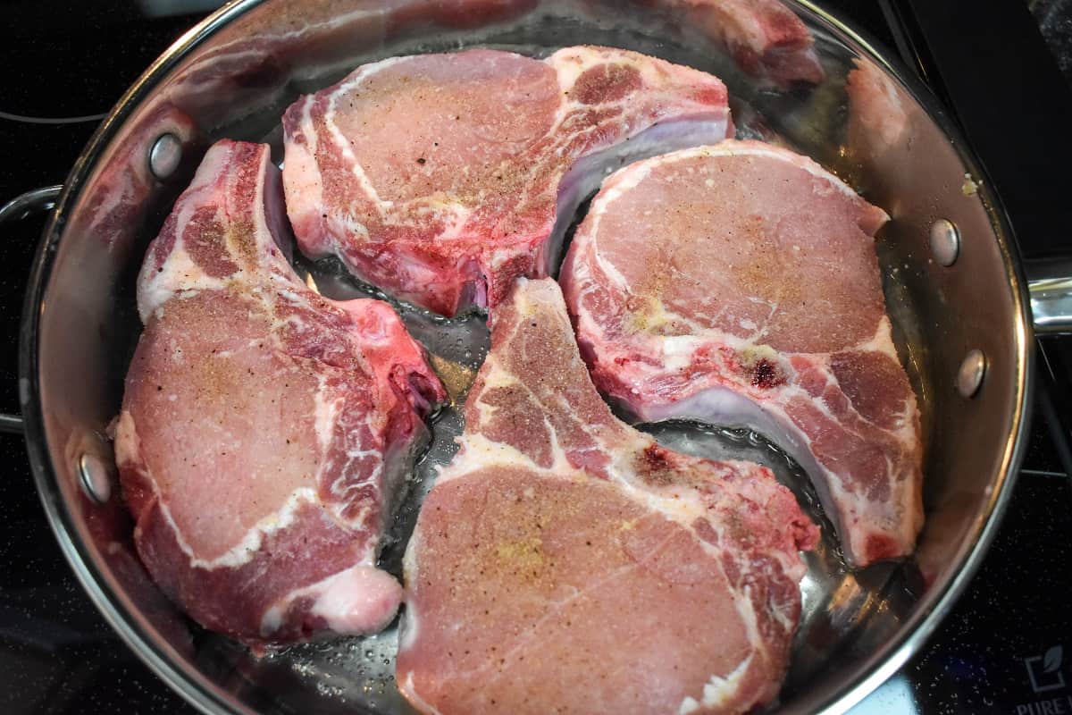 Four thick pork chops arranged in a large skillet.