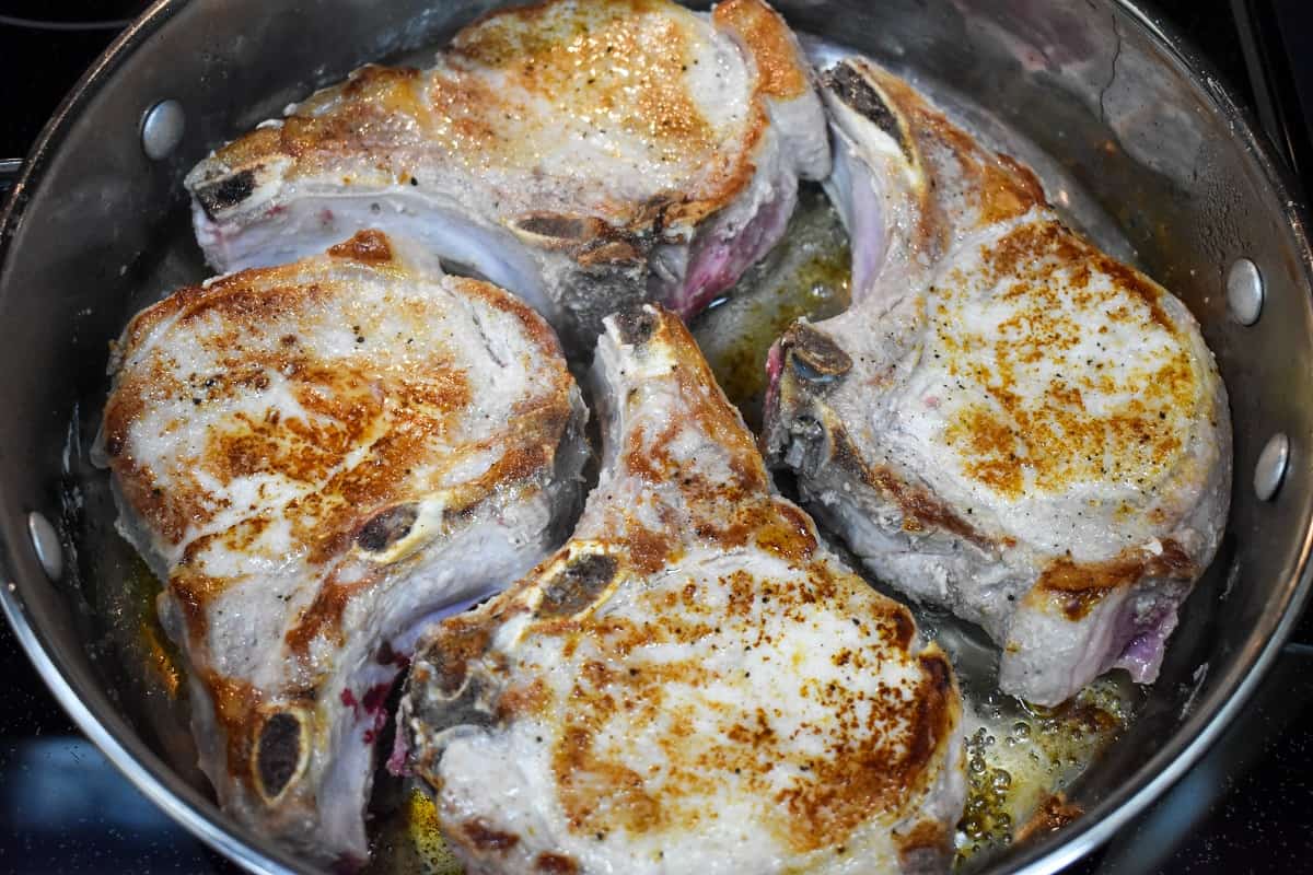 Four pork chops browning in a large skillet.