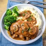 The easy one-pan chicken and mushrooms with brown gravy served with mashed potatoes and broccoli on a white plate.