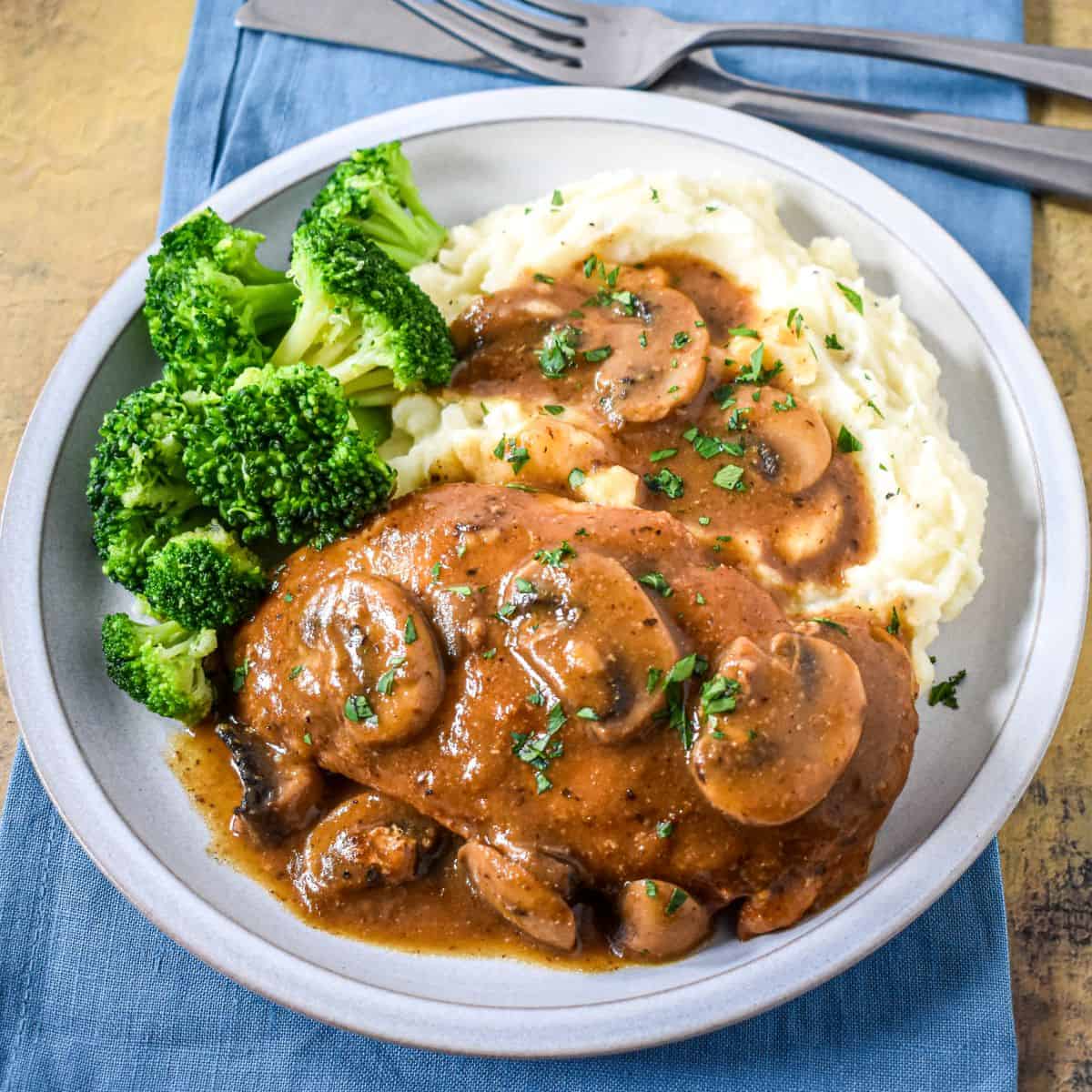 The easy one-pan chicken and mushrooms with brown gravy served with mashed potatoes and broccoli on a white plate.