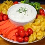 Fresh dill dip served in a white bowl surrounded with vegetables and chips