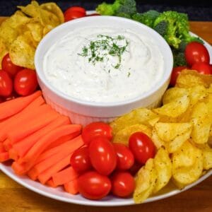 Fresh dill dip served in a white bowl surrounded with vegetables and chips