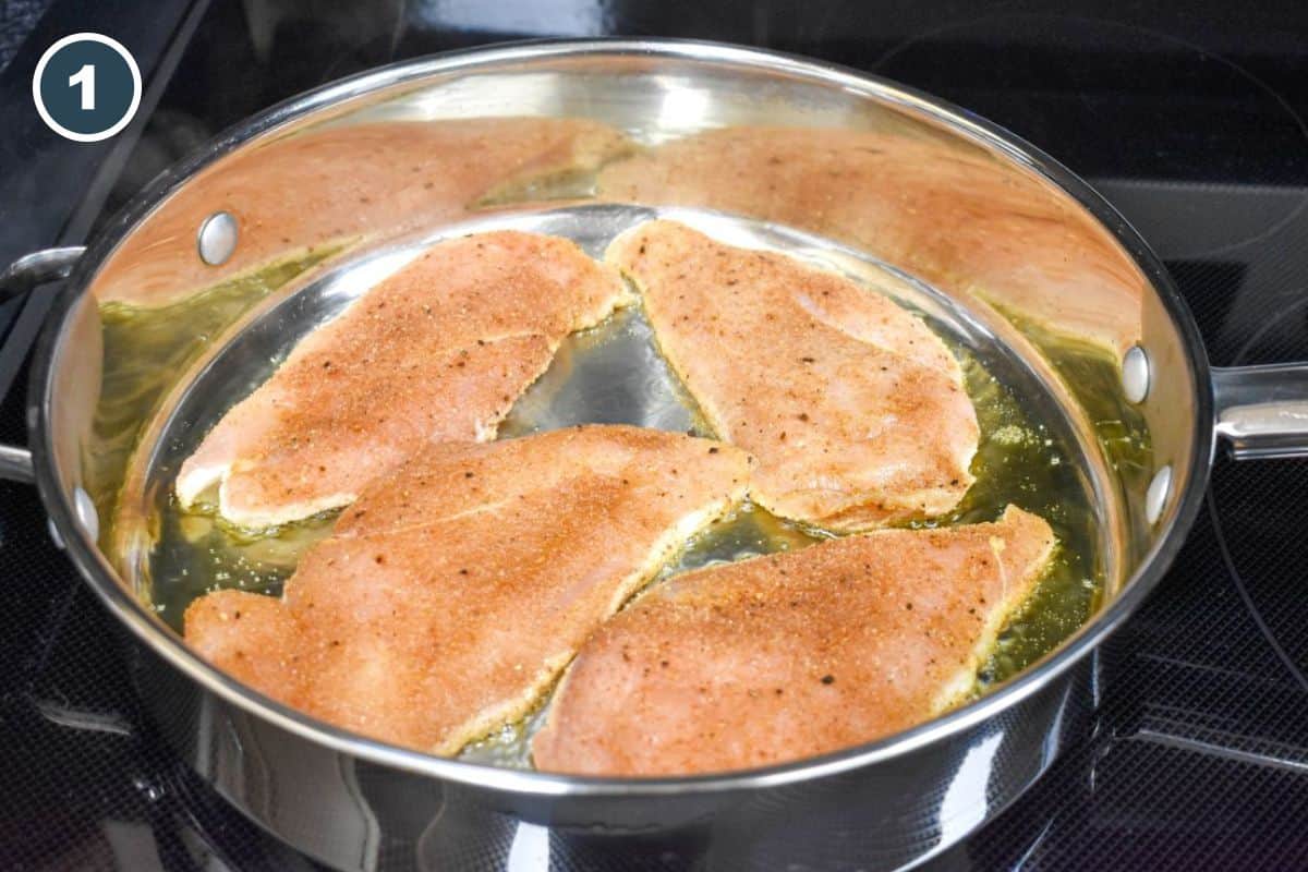 Seasoned chicken cutlets cooking in a large skillet with olive oil.