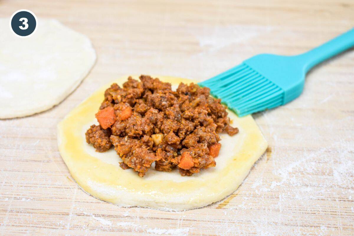 Edges of biscuit dough brushed with egg wash around the filling.