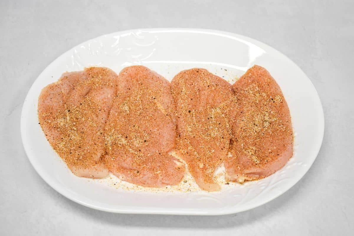 Seasoned chicken cutlets on a white plate ready for cooking.