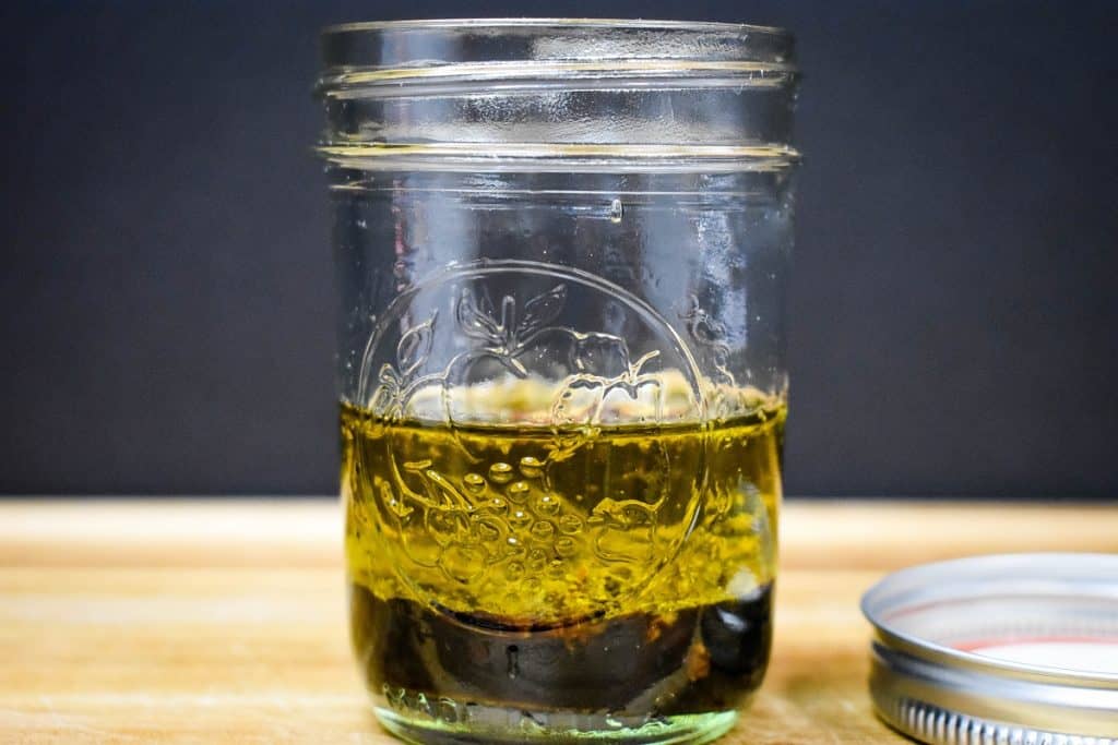 The ingredients for the salad dressing in a small canning jar before being stirred. so the oil and balsamic vinegar are separated.