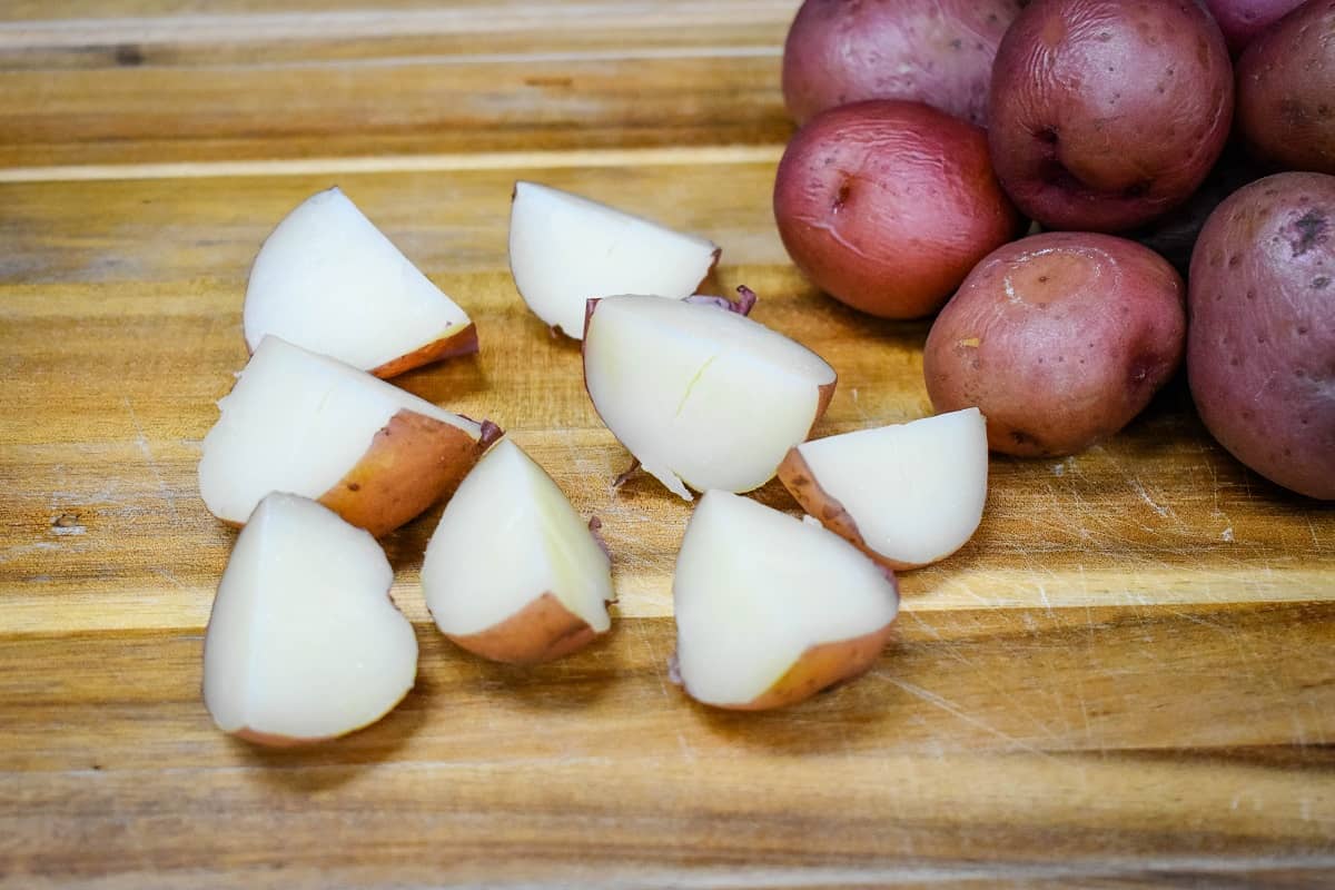 Cooked small red potatoes cut into quarters on a wood cutting board.