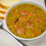 Lentils with andouille sausage soup served in a light gray bowl with bread slices in the background.