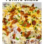 A close up image of loaded potato salad garnished with chopped bacon, shredded cheese and chopped chives.