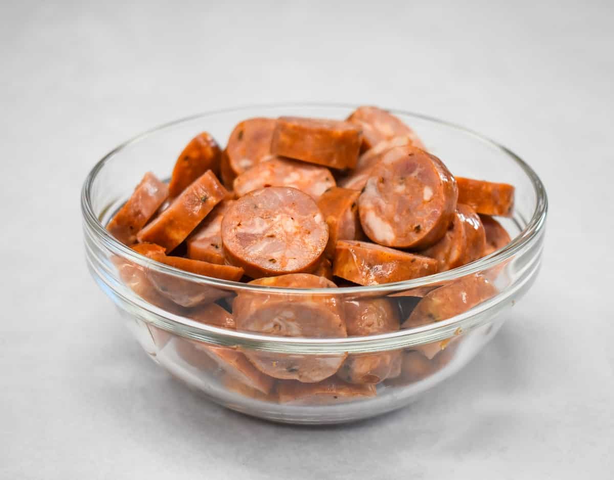 An image of sliced andouille sausage in a glass bowl set on a white table.