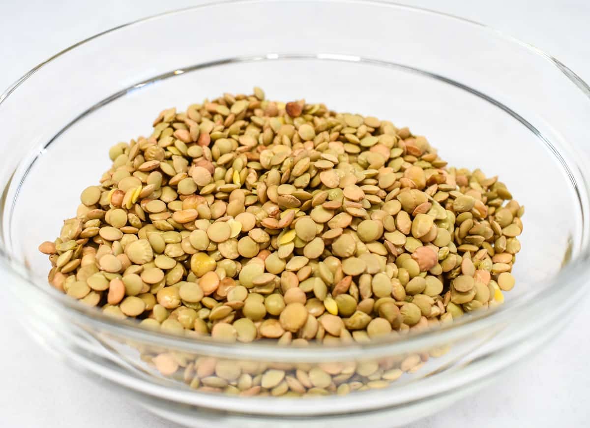An image of dry lentils in a glass bowl set on a white table.
