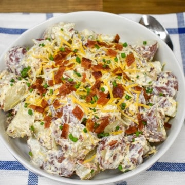 An image of loaded potato salad served in a large white bowl and garnished with bacon, cheese, and chives.