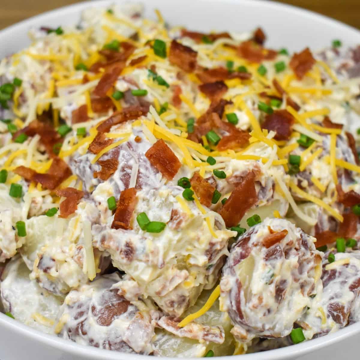 A close up image of the finished potato salad garnished with bacon, cheese, and chives.