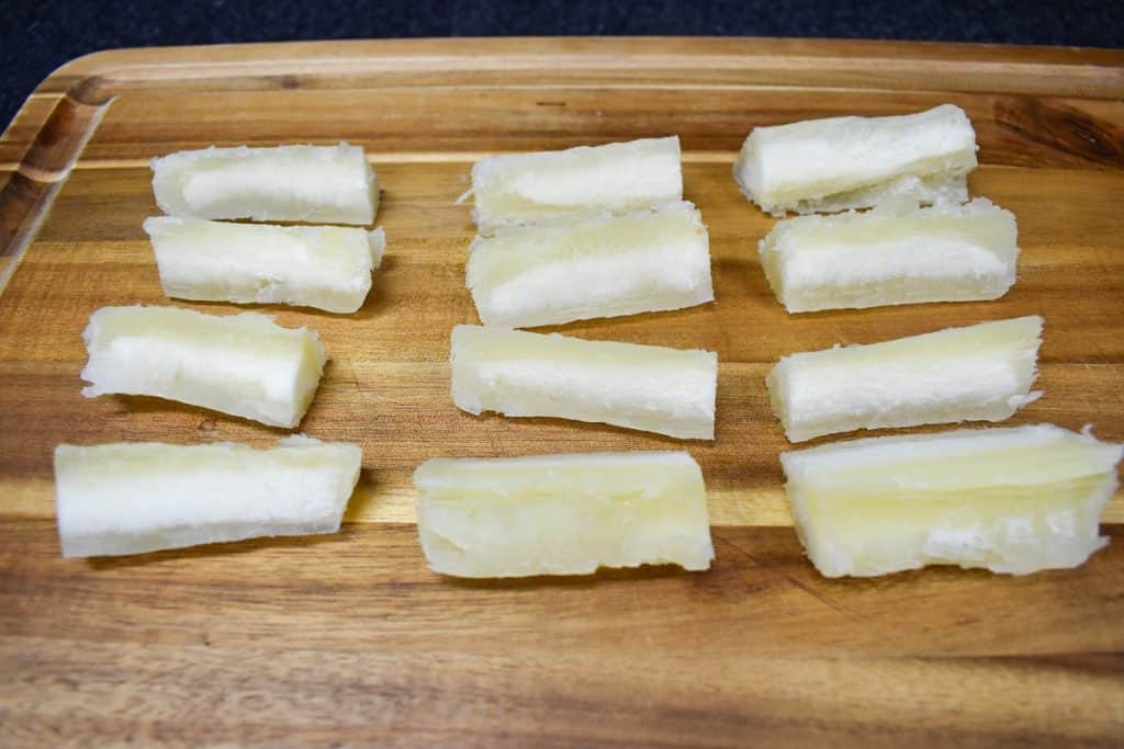 Cook yuca cut into thick pieces displayed on a wood cutting board.