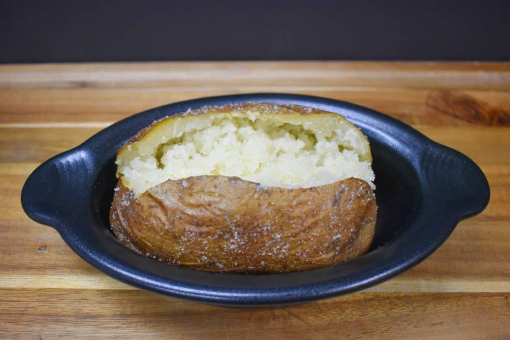 A large baked potato that opened in the center displayed in a small black crock.