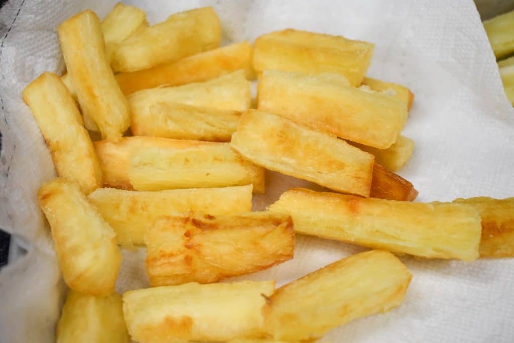 Fried yuca pieces displayed draining on a white paper towel.