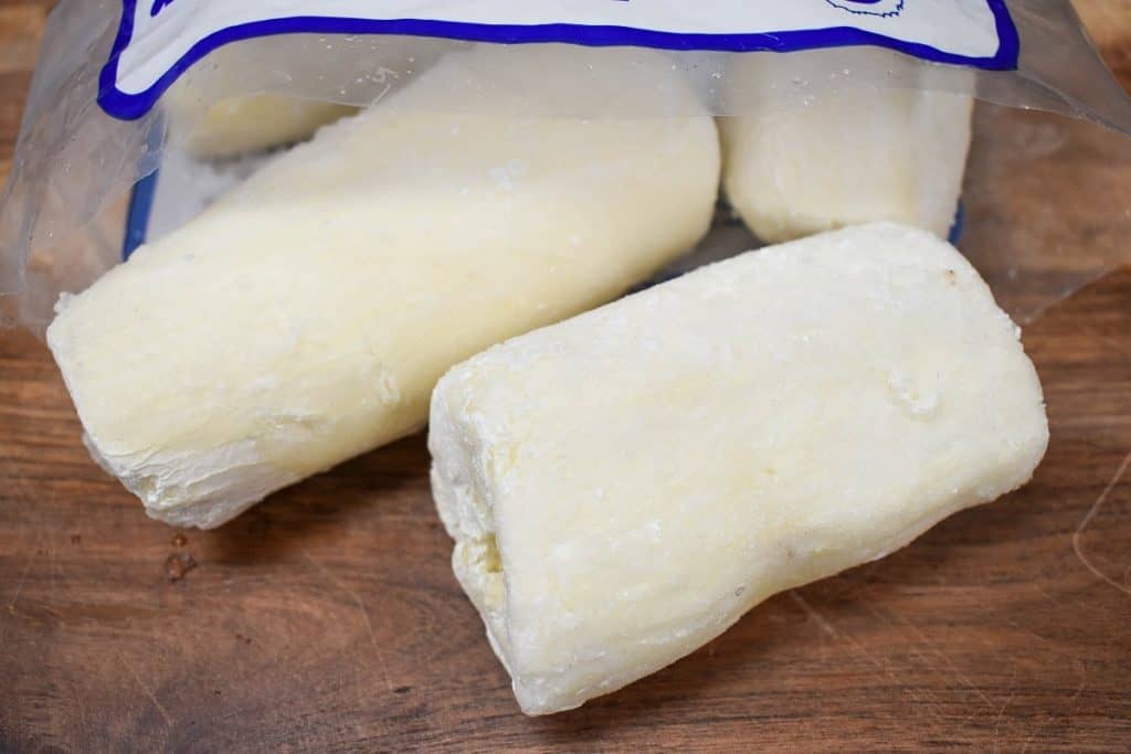 Two large pieces of frozen yuca displayed on a wood cutting board.